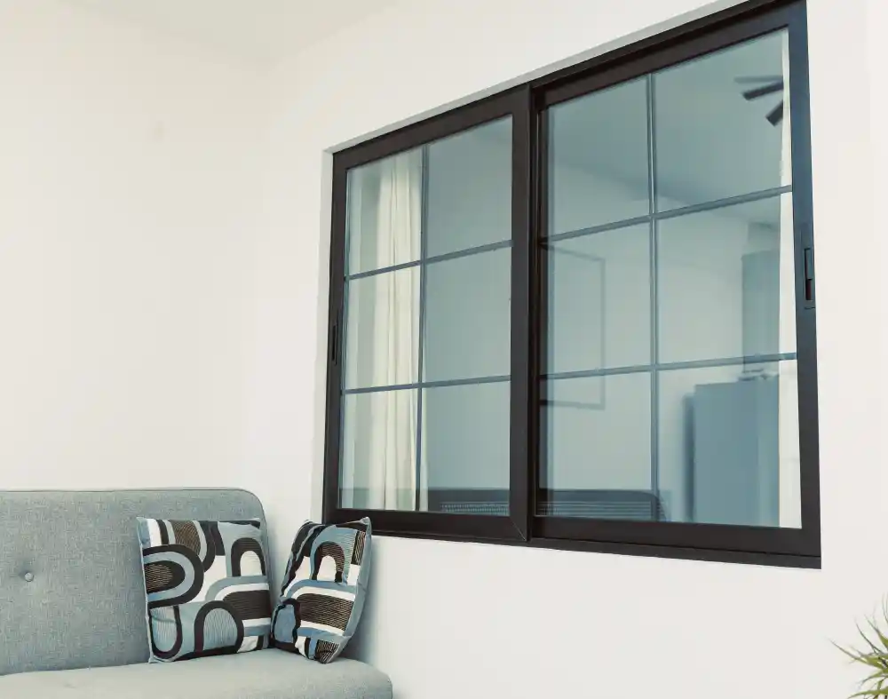Modern black sliding window with grid design installed in a living room by a leading UPVC & Aluminium windows manufacturer in Vadodara.